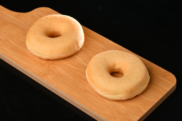 Dos donuts en una tabla de madera sobre una mesa negra