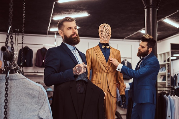 Dos elegantes asistentes de tienda elegantemente vestidos que trabajan en una tienda de ropa masculina.