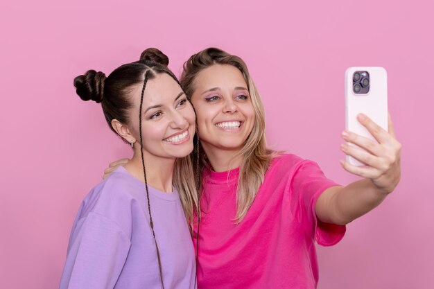 Dos elegantes y atractivas chicas morenas y rubias sonrientes tomando una selfie en el teléfono móvil