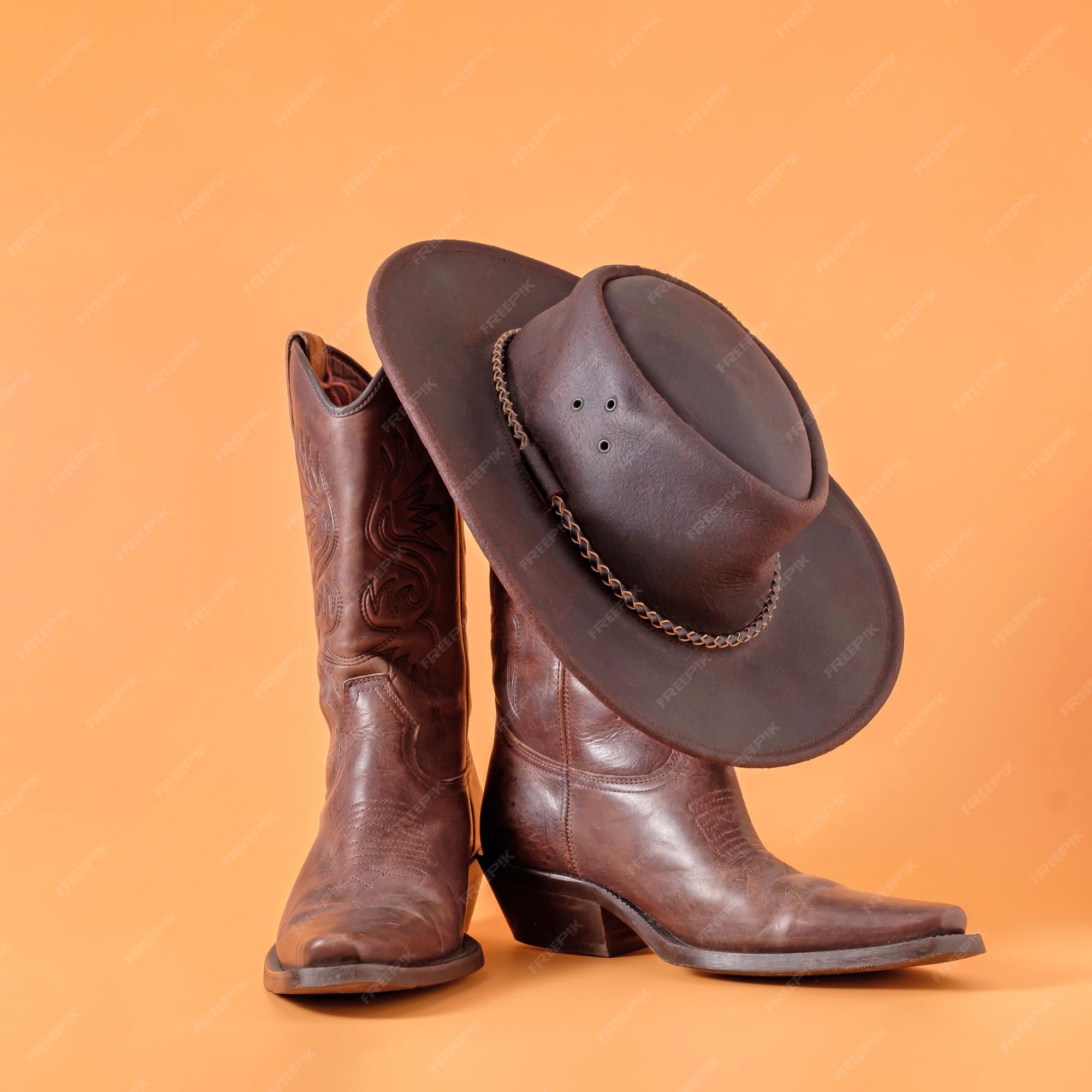 Dos elegantes botas clásicas y un sombrero stetson de vaquero de cuero sobre un fondo de arcilla naranja de vaquero ranger en un rancho en estados unidos, texas | Foto Premium