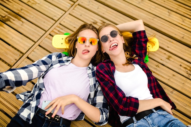 Dos elegantes jóvenes urbanas con longboards yacen en el suelo de madera de la calle. Los amigos se divierten y pasan tiempo juntos en el verano durante las vacaciones.