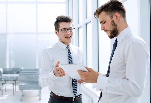 Dos empleados con una tableta digital discutiendo algo de pie en la foto de la oficina con espacio para copiar