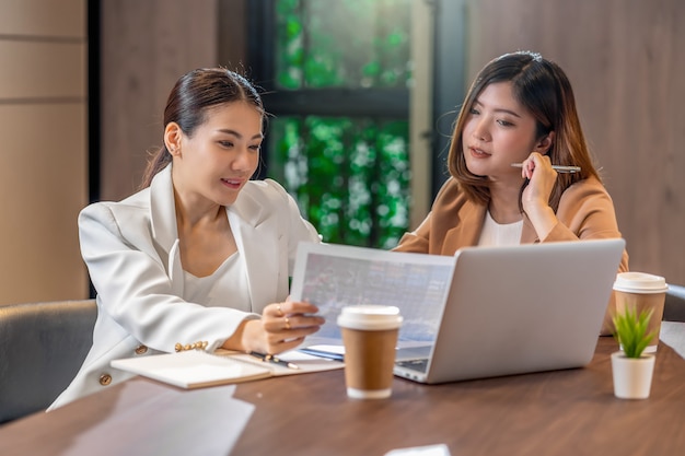 Dos empresarias asiáticas que trabajan con la empresa asociada con documento gráfico en papel y computadora portátil con tecnología en la moderna sala de reuniones