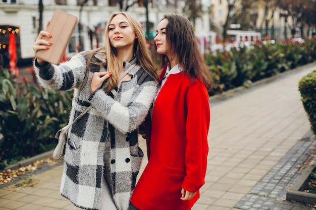 Dos empresarias con estilo jovenes que se colocan en una ciudad del otoño y utilizan la tableta