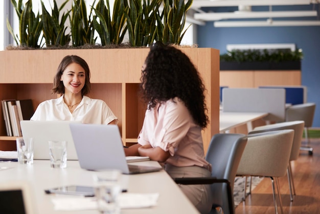 Dos empresarias que trabajan en computadoras portátiles sentadas a la mesa en la moderna oficina abierta