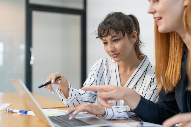 Dos empresarias que usan computadoras portátiles discuten documentos de informes de marketing para reuniones de equipos de negocios