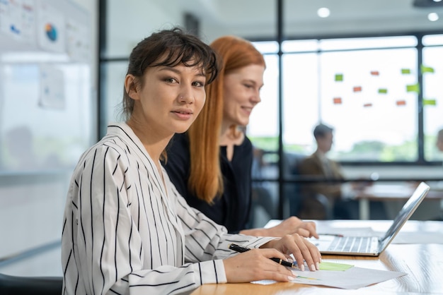 Dos empresarias que usan computadoras portátiles discuten documentos de informes de marketing para reuniones de equipos de negocios