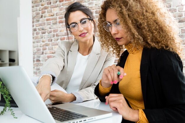 Dos empresarias trabajando con ordenador portátil en su oficina.