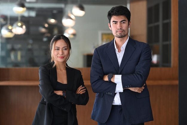Dos empresarios exitosos en ropa formal de pie con los brazos cruzados en la oficina moderna