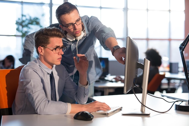 dos empresarios que usan computadoras preparándose para la próxima reunión y discutiendo ideas con colegas en segundo plano