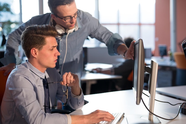 Foto dos empresarios que usan computadoras preparándose para la próxima reunión y discutiendo ideas con colegas en segundo plano