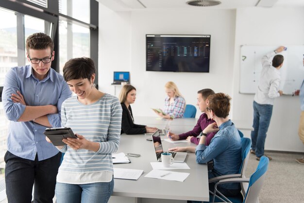 dos empresarios que usan una tableta preparándose para la próxima reunión y discutiendo ideas con colegas en segundo plano