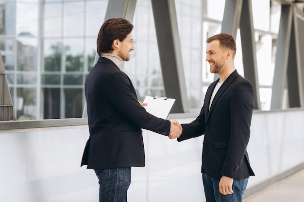 Dos empresarios sonriendo entre sí están trabajando de la mano para presentar a la reunión en el trabajo sobre el fondo de los edificios urbanos