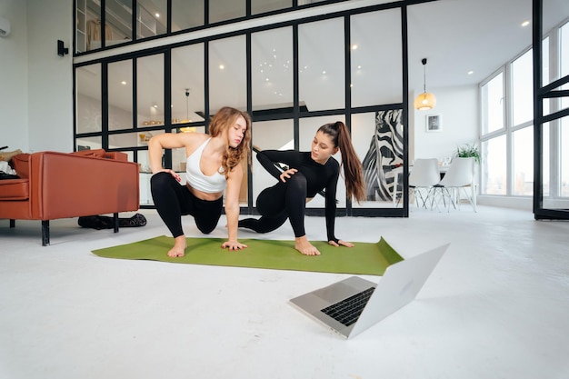 Dos encantadoras deportistas hacen ejercicios de poses de yoga en casa