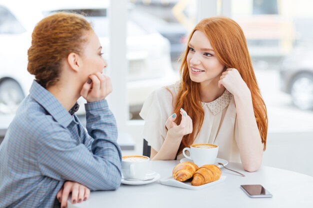 Dos encantadoras mujeres jóvenes tomando café y hablando en el café