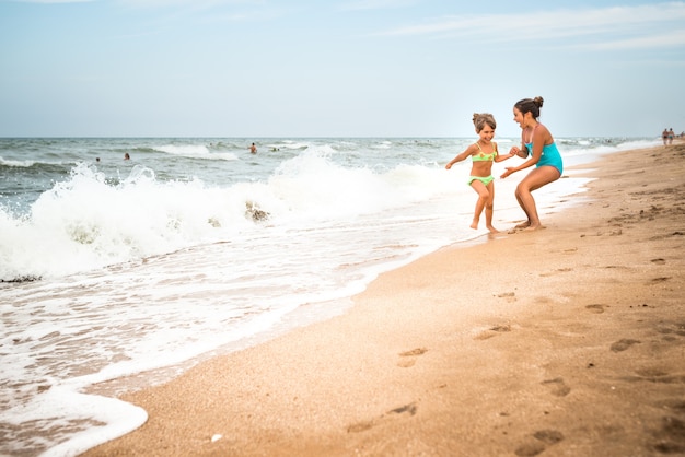 Dos encantadoras niñas en traje de baño bailan en una playa de arena cerca del mar contra el cielo azul en un cálido día de verano. Concepto de vacaciones con niños