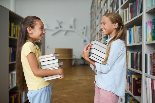 Dos escolares alegres sosteniendo montones de libros en sus manos