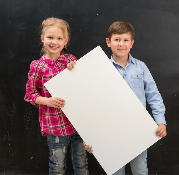 Dos escolares sonrientes con una hoja de papel en blanco