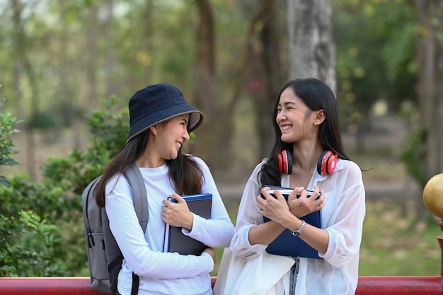 Dos estudiante universitario feliz hablando y riendo mientras está de pie en el parque en el campus