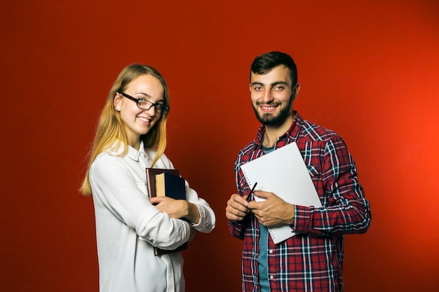 Dos estudiantes adolescentes mirando a la cámara sosteniendo libros sobre fondo rojo.