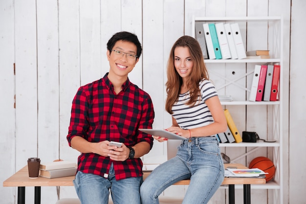 Dos estudiantes felices sentados en la mesa mientras sostienen el teléfono celular y la tableta