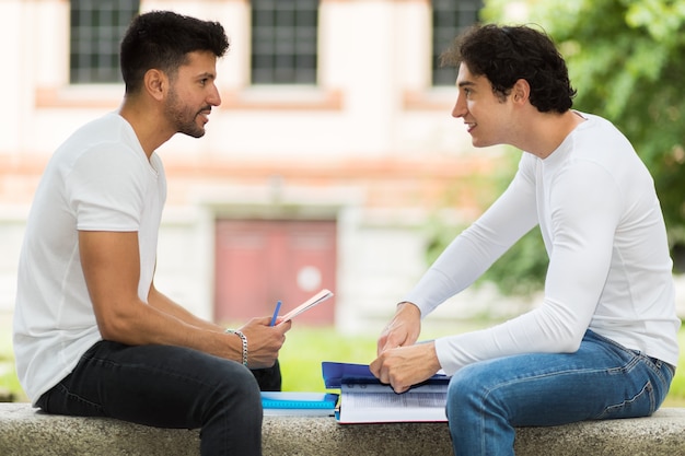 Foto dos estudiantes que estudian juntos sentados en un banco al aire libre