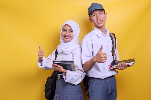 Dos estudiantes de secundaria indonesios en uniforme blanco y gris sosteniendo libros mientras levantan los pulgares