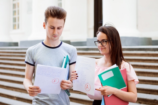 Dos estudiantes, sosteniendo hojas de papel con resultados de pruebas.