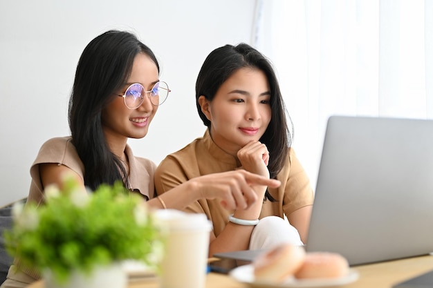 Dos estudiantes universitarias asiáticas enfocadas y concentradas haciendo tareas de trabajo en una computadora portátil juntas