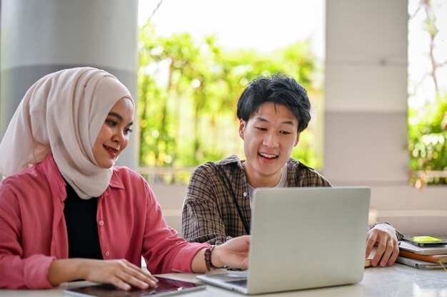 Dos estudiantes universitarios asiáticos están mirando la pantalla de una computadora portátil discutiendo e intercambiando ideas