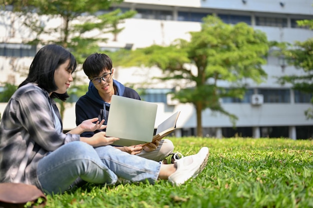 Dos estudiantes universitarios asiáticos están trabajando juntos en el trabajo escolar en el parque del campus