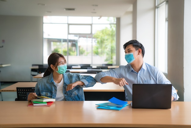 Dos estudiantes universitarios asiáticos con mascarilla reunión y saludo amigo tocando el codo