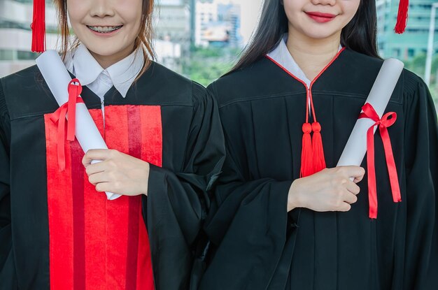 Dos estudiantes universitarios mujer asiática usan batas y tienen diploma de graduación