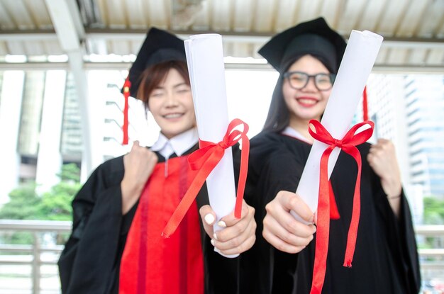Dos estudiantes universitarios mujer asiática usan batas tienen diploma de graduación