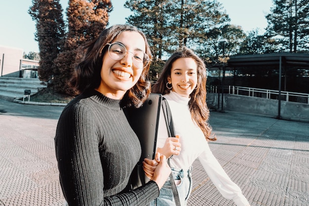 Dos estudiantes universitarios que van a su clase mientras hablan y hablan sonriendo a la cámara. Sosteniendo una mochila portátil. Ríete, ama el concepto de amistad. Nueva carrera, grado o estudio. Niñas bereberes africanas estudiando