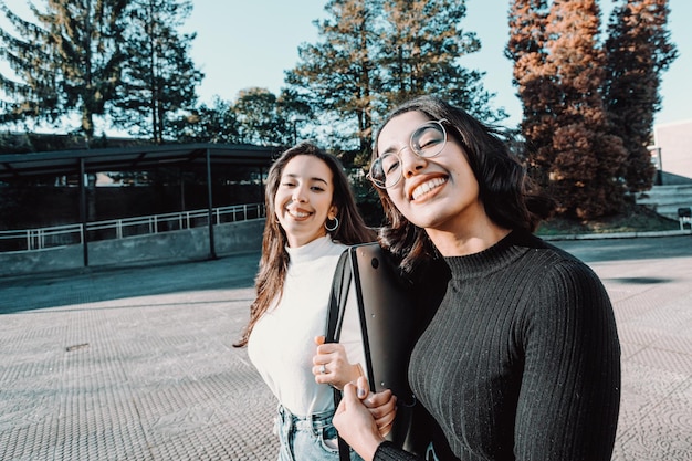 Dos estudiantes universitarios que van a su clase mientras hablan y hablan sonriendo a la cámara. Sosteniendo una mochila portátil. Ríete, ama el concepto de amistad. Nueva carrera, grado o estudio. Niñas bereberes africanas estudiando