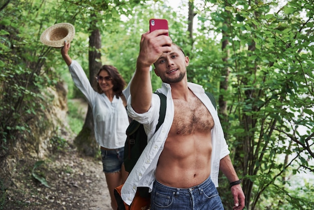 Dos excursionistas con mochilas en la espalda en la naturaleza. Pareja joven hombre y mujer hacen selfie foto a pie en un día de verano