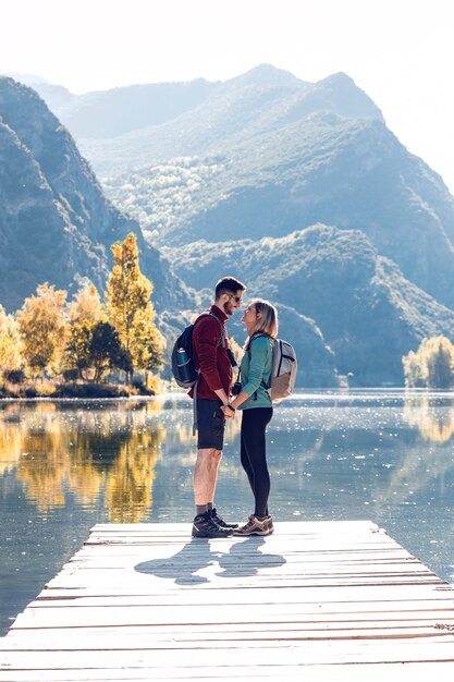 Dos excursionistas de viaje enamorados besándose frente al lago en la montaña.