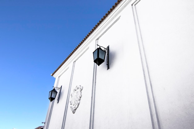 Dos farolas negras colgando en una fachada blanca Un cielo azul en el fondo