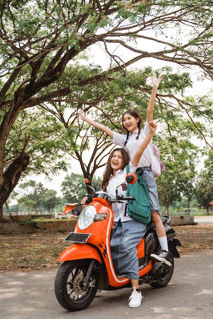 Dos felices chicas de secundaria montando una moto imprudente mientras celebraban la graduación en la calle