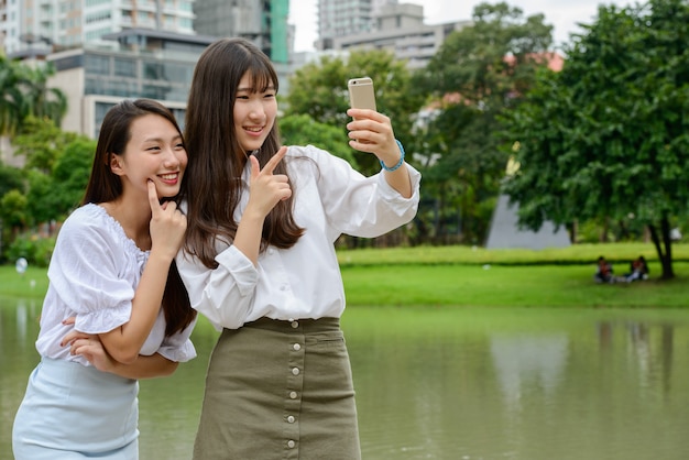 Dos felices jóvenes hermosas mujeres adolescentes asiáticas tomando selfie juntos en el parque