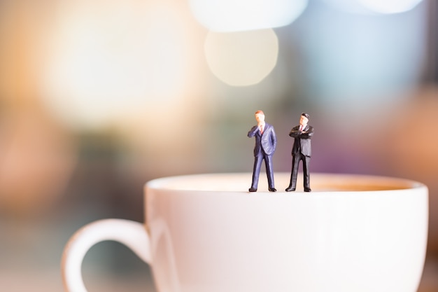 Dos figuras en miniatura de los hombres de negocios se colocan y piensan en un plato blanco de café caliente.