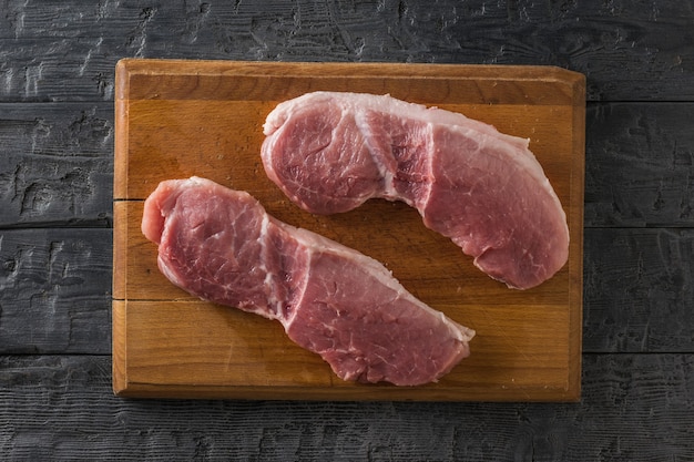 Dos filetes de cerdo en una tabla de cortar de madera sobre una mesa de madera. Ingredientes para cocinar platos de carne.