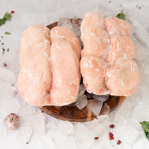 Dos filetes de pollo crudos se sientan en un tazón de madera con hielo y pimiento rojo encima.