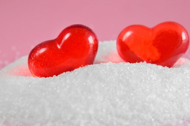 Dos formas de corazón rojo sobre sal blanca sobre fondo rosa primer plano vacaciones de todos los amantes el 14 de febrero