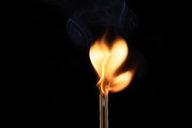 Dos fósforos llameantes con humo y fuego en forma de corazón
