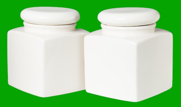 Dos frascos de cerámica blanca para el almacenamiento de alimentos en la cocina se aíslan sobre un fondo verde