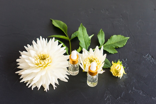 Dos frascos de cosméticos de vidrio transparente con ácido healcrónico sobre un fondo negro con flores blancas. el concepto de belleza y cuidado de la piel.