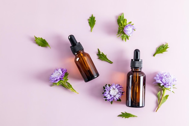 Dos frascos cuentagotas de vidrio para uso cosmético y flores moradas sobre un fondo morado prevención de cambios en la piel relacionados con la edad vista superior