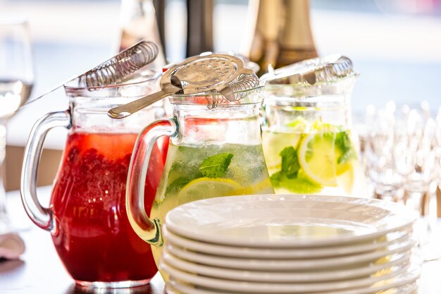 Dos frascos de vidrio de limonada de frambuesa fresca hecha en casa o cóctel de mojito virgen con una pajita sobre la mesa entre los platos preparados para servir